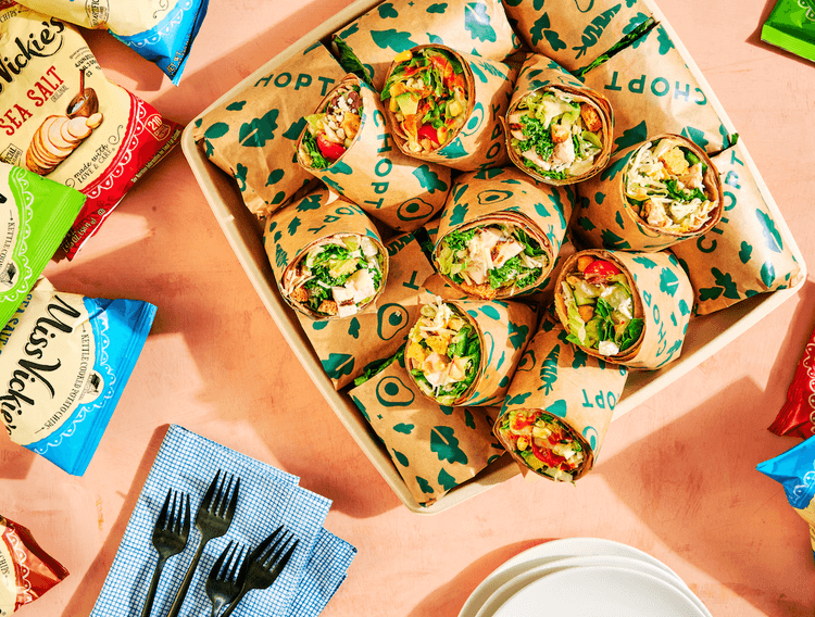 A platter of wraps surrounded by bags of chips